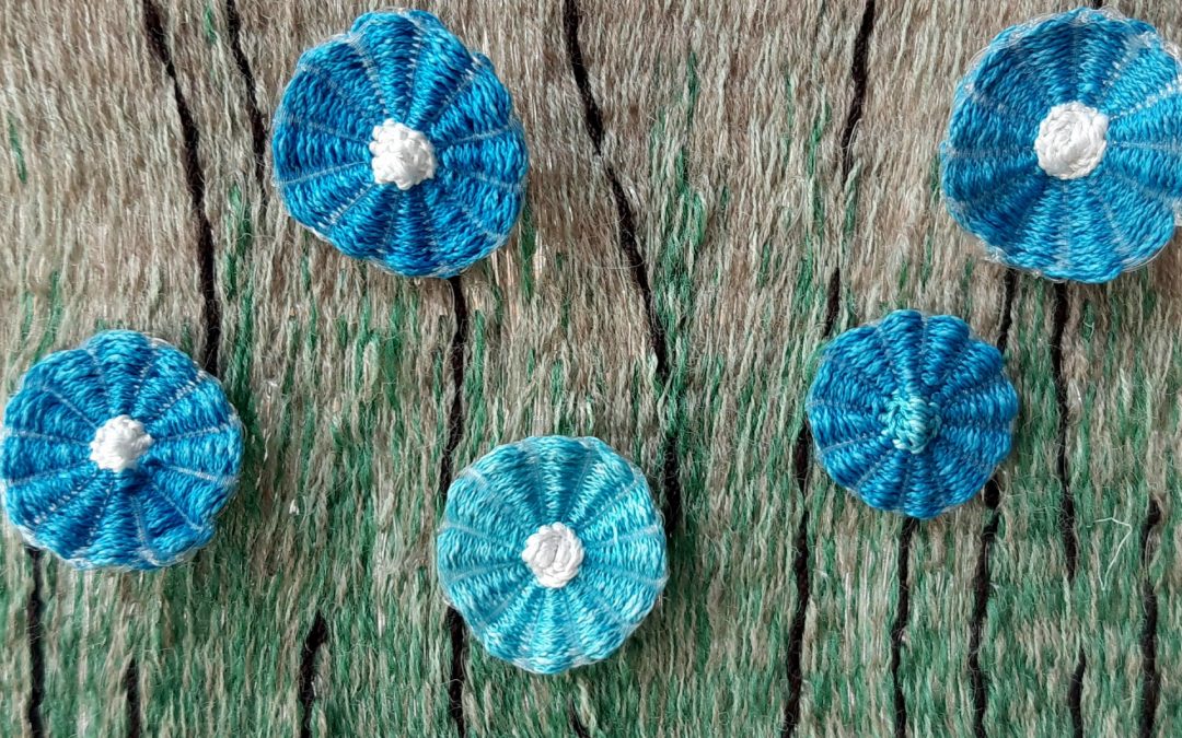 5 Blue woven flowers embedded in a grey and green woven tapestry background
