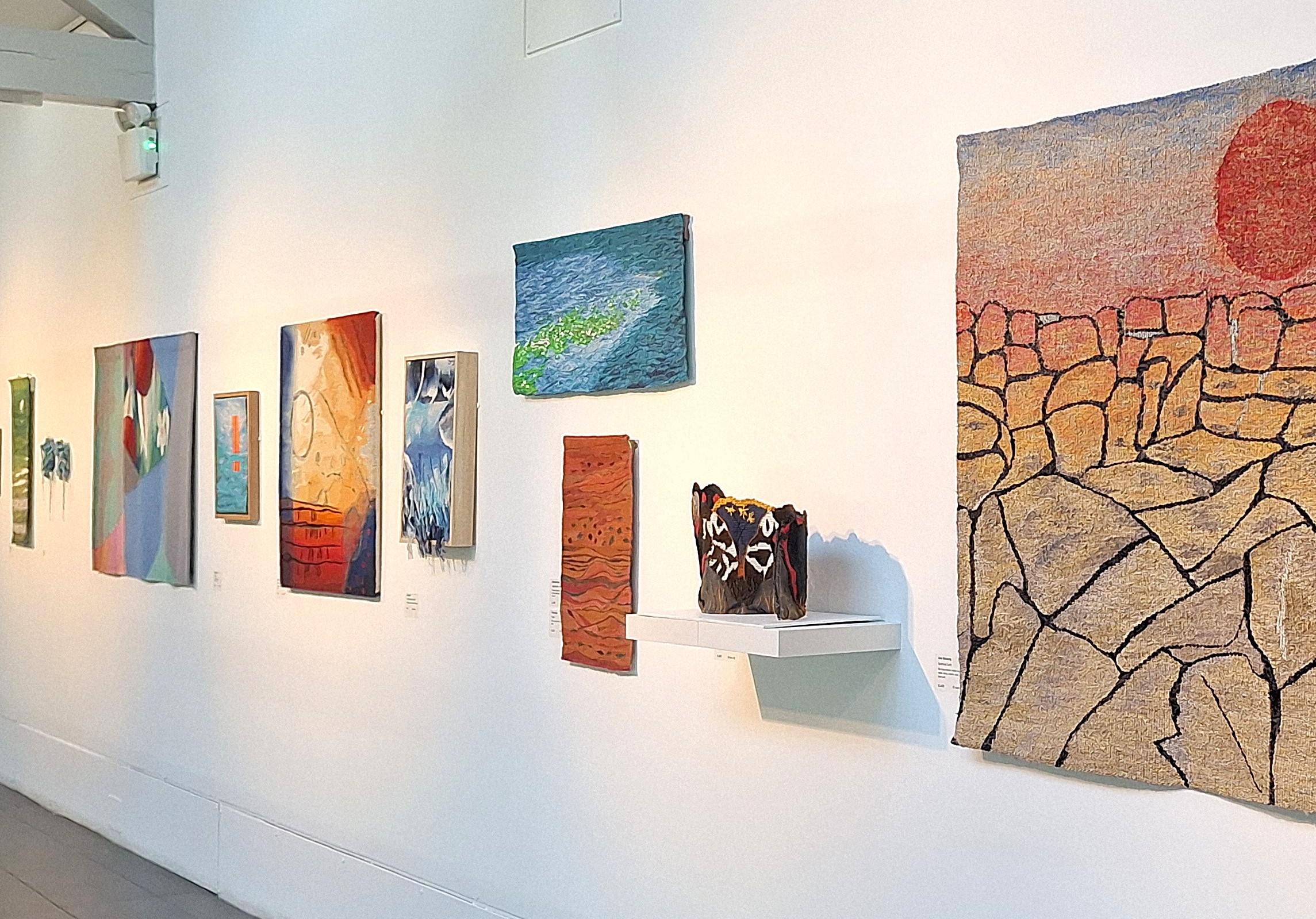 The 3D tapestry 'Hunting Tigers and Woolly Bears' displayed on a shelf alongside other artists' works in the British Tapestry Group exhibition at Dovecot Studios in Edinburgh