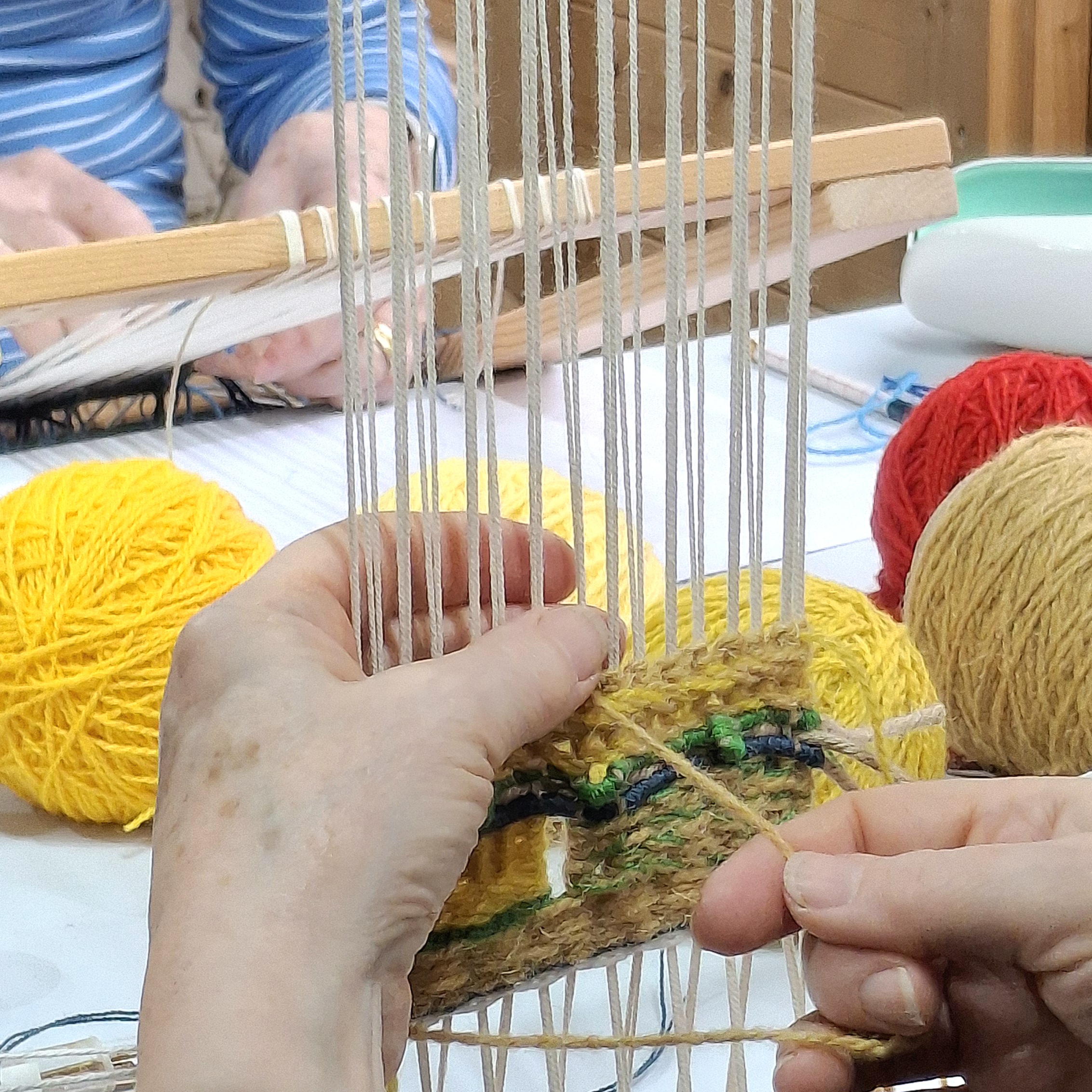 A participant practicing tapestry weaving techniques, at a Lucy Sugden tapestry workshop, featuring frame looms and vibrant wool yarns.